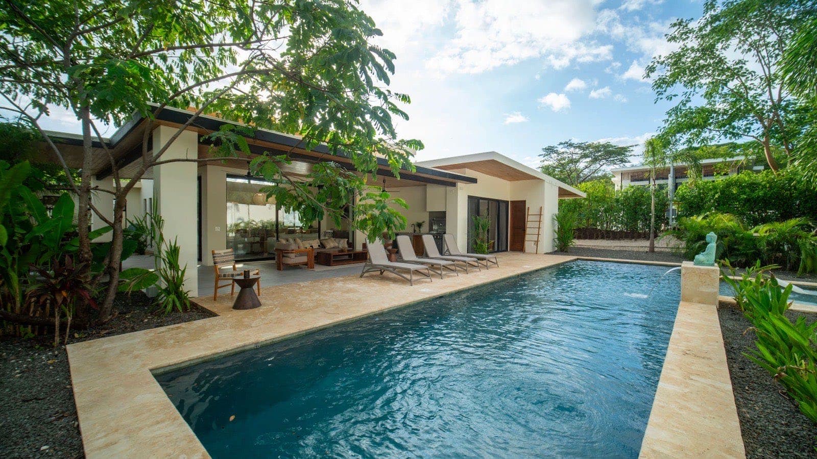 The 44-foot pool seen lengthwise, sun loungers on the travertine deck, and a turquoise seated Buddha spouting water into the water